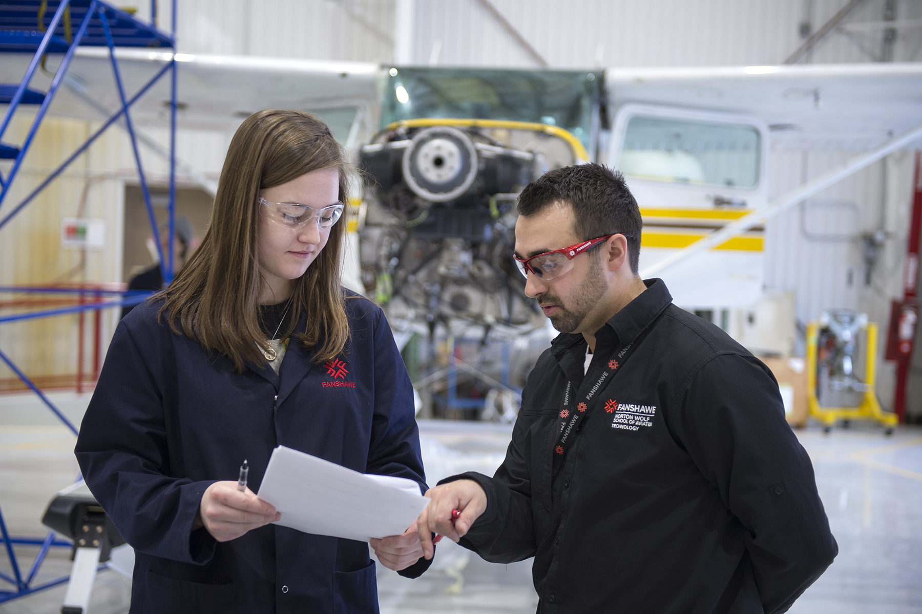 A student and instructor review documents at Fanshawe College's maintenance hangar